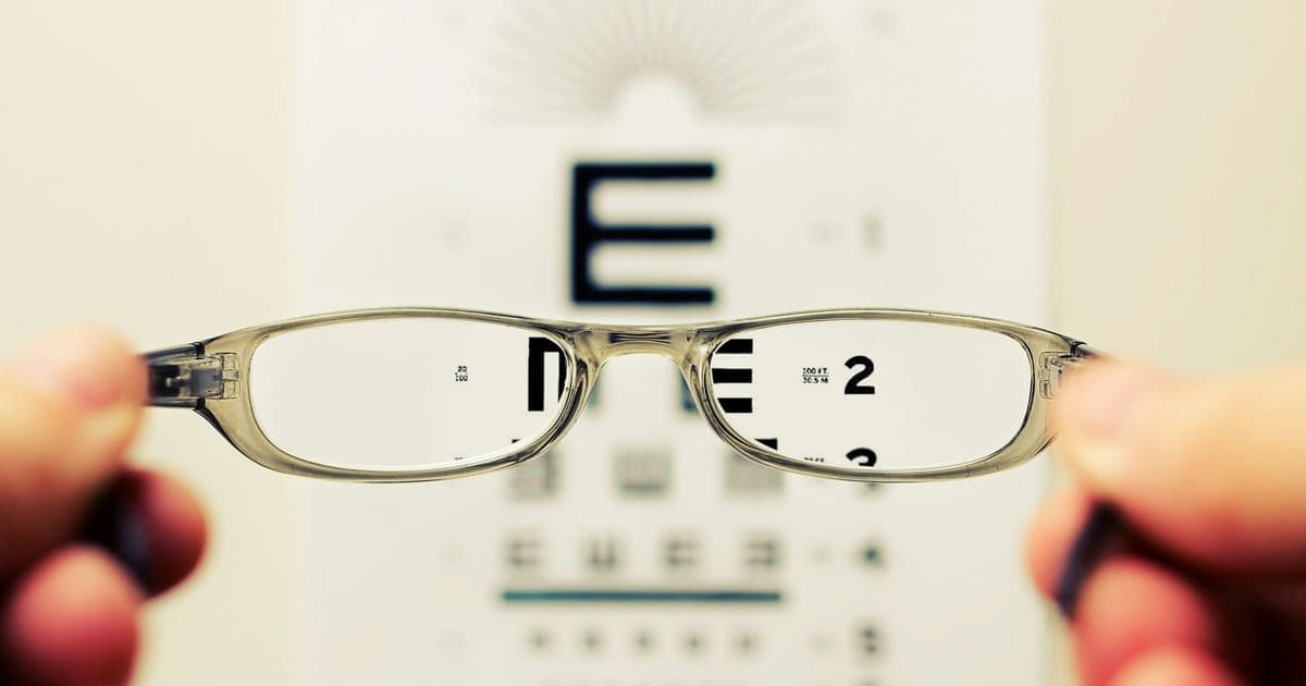 Glasses held up in front of an eye-test chart, the letters sharp through the lenses and blurred around them